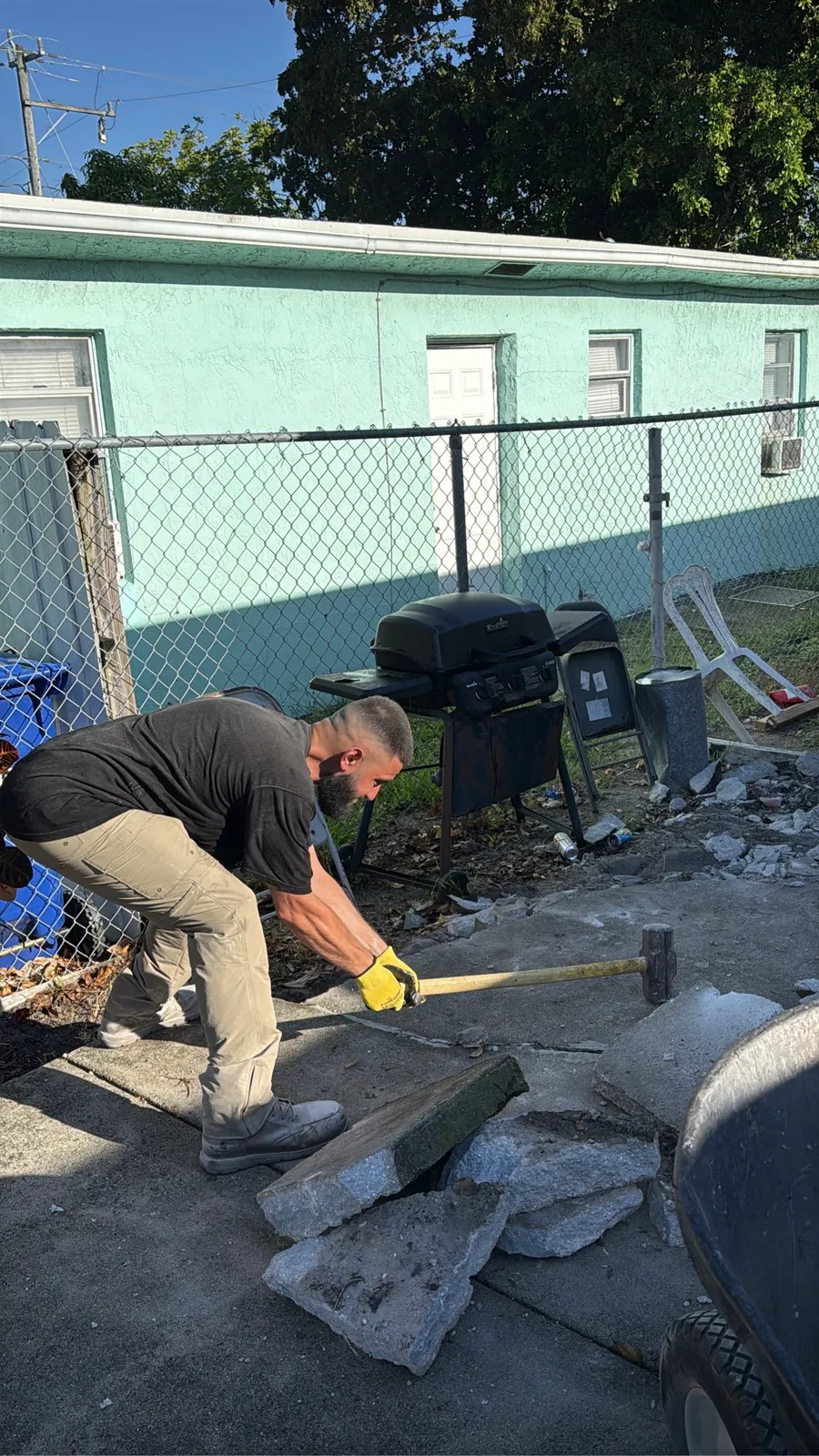 Worker breaking up a concrete patio with a sledgehammer in Broward County FL